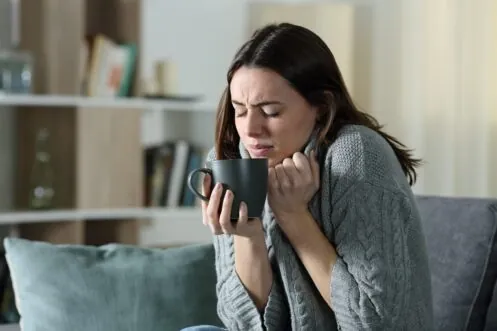 Woman wrapped in a sweater holding a warm mug in a chilly home